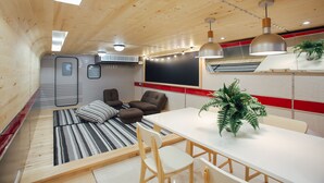 Quarto compacto com cama, mesa de jantar e cadeiras. Uma janela grande oferece iluminação natural, e um ventilador de teto é visível.