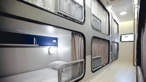 Um vagão de trem com beliches, uma parede azul e uma janela com cortinas.
