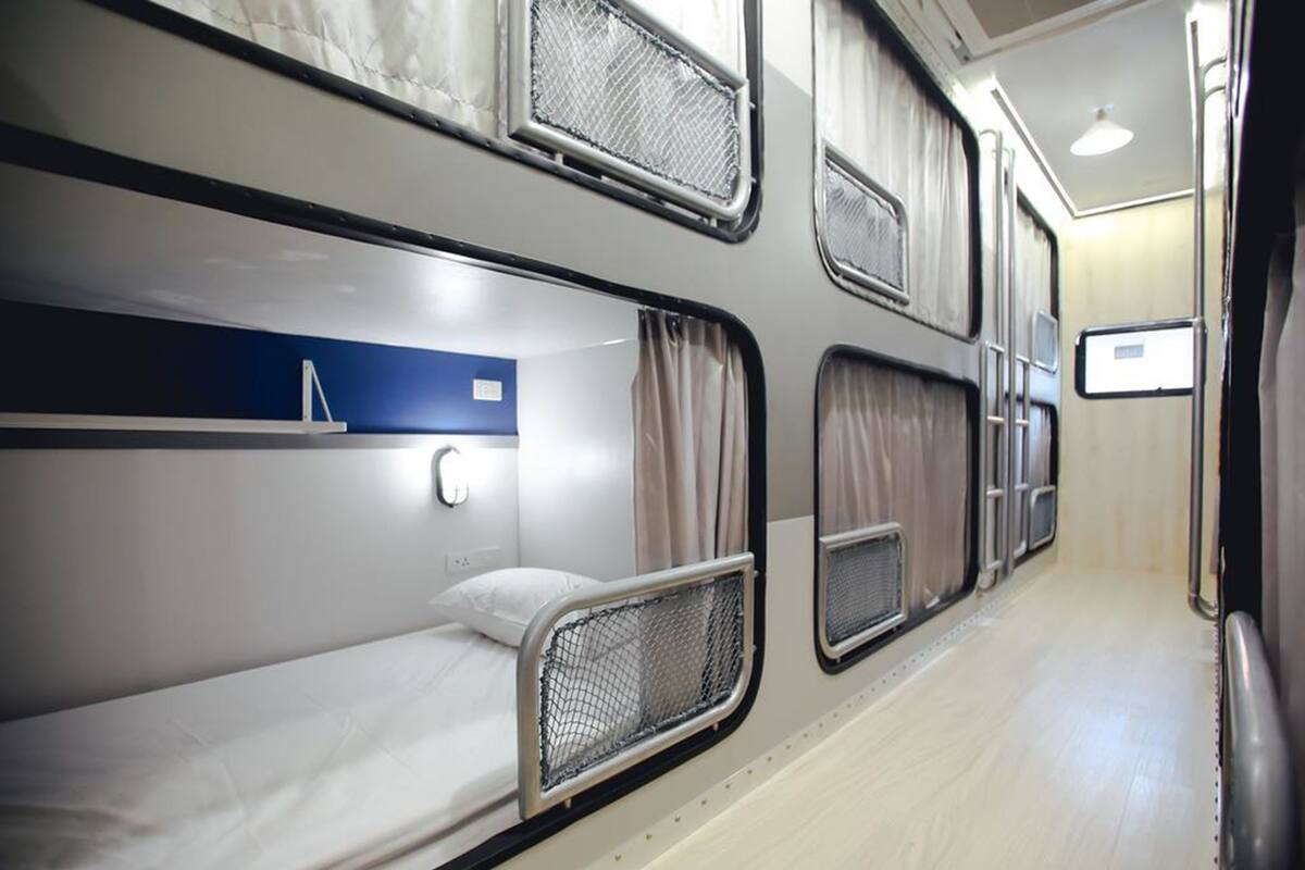 Un compartiment de train avec des lits superposés, un mur bleu et une fenêtre avec des rideaux.