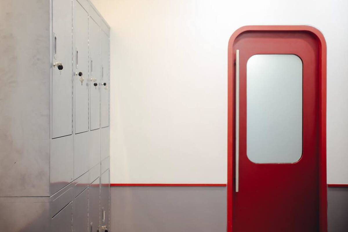 Un couloir avec une porte rouge et un espace réservé aux casiers, de couleur grise.