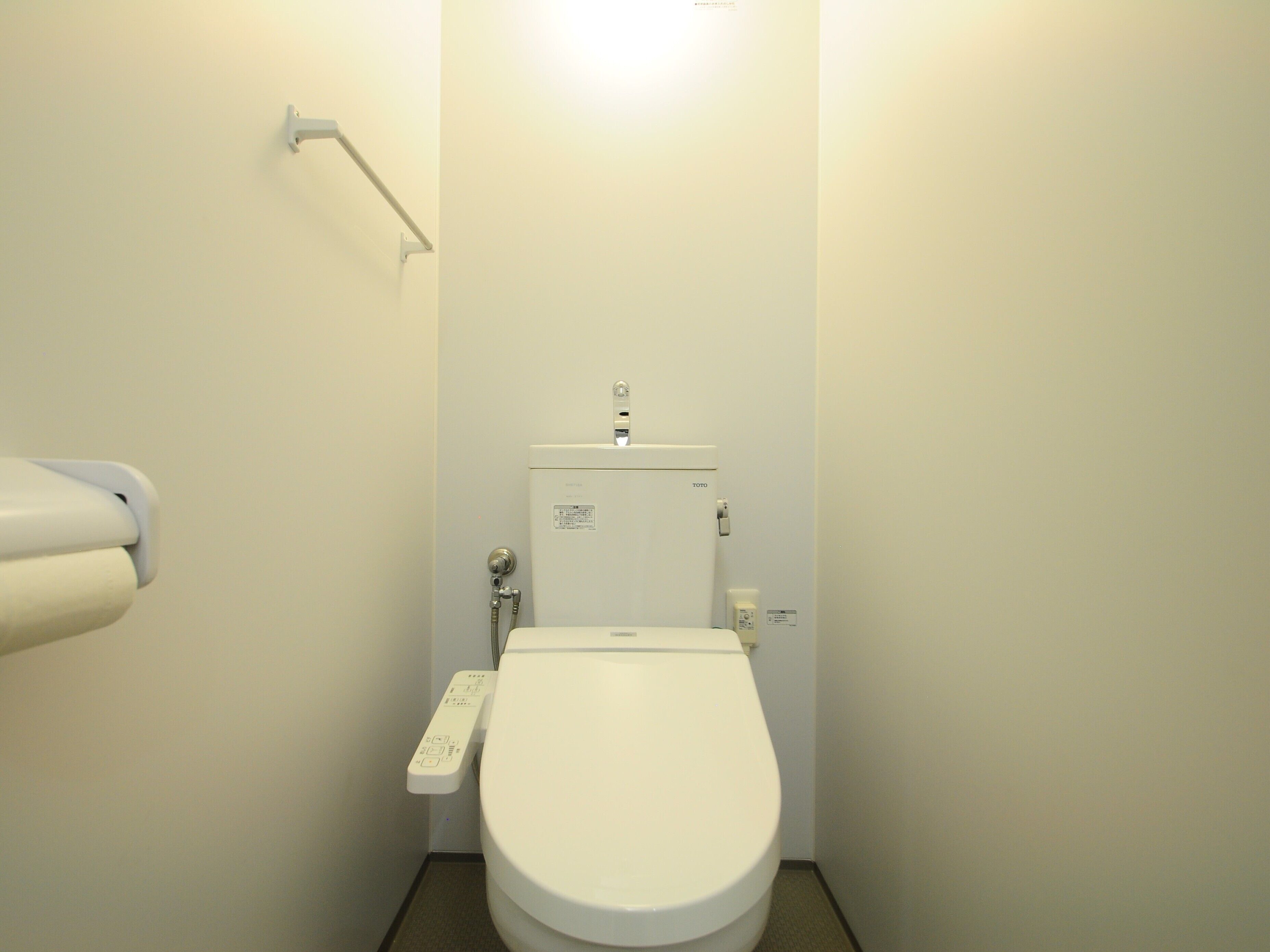 A small, white bathroom with a toilet, a hand dryer, and a wall-mounted towel rack.