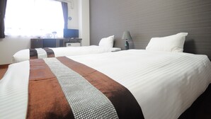 Ein Hotelzimmer mit zwei Betten, einem Schreibtisch, einer Lampe und einer Klimaanlage.