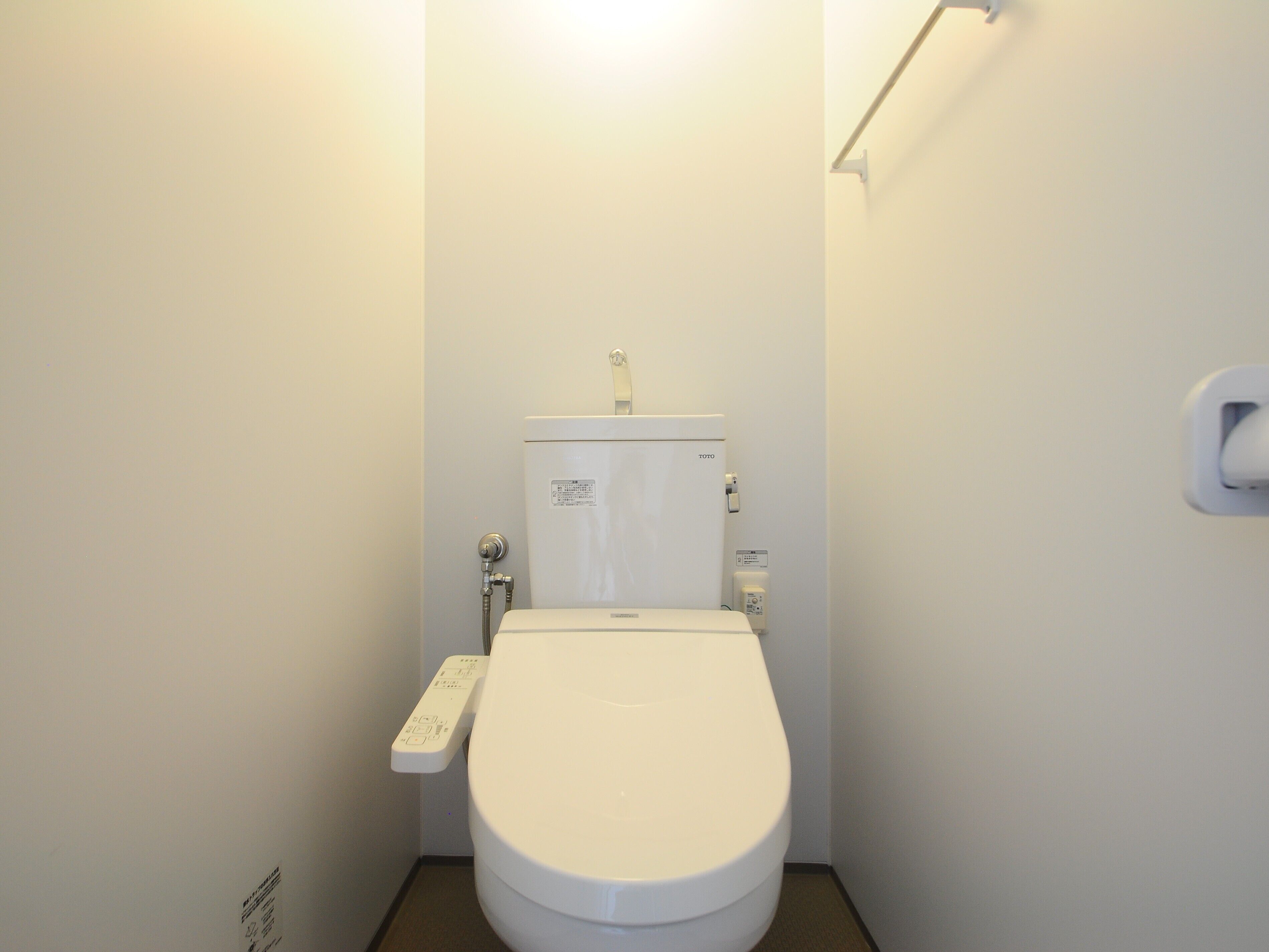 Et lille, hvidt toilet med et kontrolpanel på venstre side, en TOTO tank, og et vægmonteret skyllehåndtag på højre side.