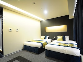 Habitación de hotel con dos camas, un ventanal con cortinas, una lámpara fijada a la pared y piso alfombrado.