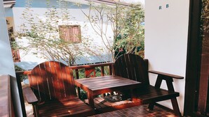 A wooden outdoor seating area with a table and chairs, a tiled floor, and a view of a building with a window and plants. - Rung Arun Resort (Ko Pha-ngan)