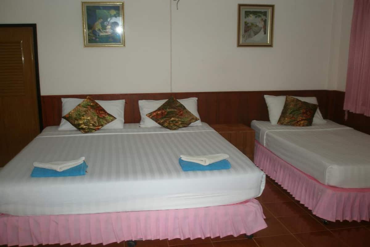 Ein Hotelzimmer mit zwei Betten, jeweils mit weißer Matratze und rosa Bettdecke. Auf den Betten liegen dekorative Kissen und gefaltete Handtücher. Das Zimmer hat ein Holz-Kopfteil und eine Tür links.