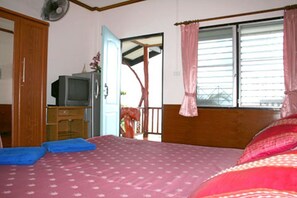 A bedroom with a bed, a television on a wooden cabinet, and a window with curtains.