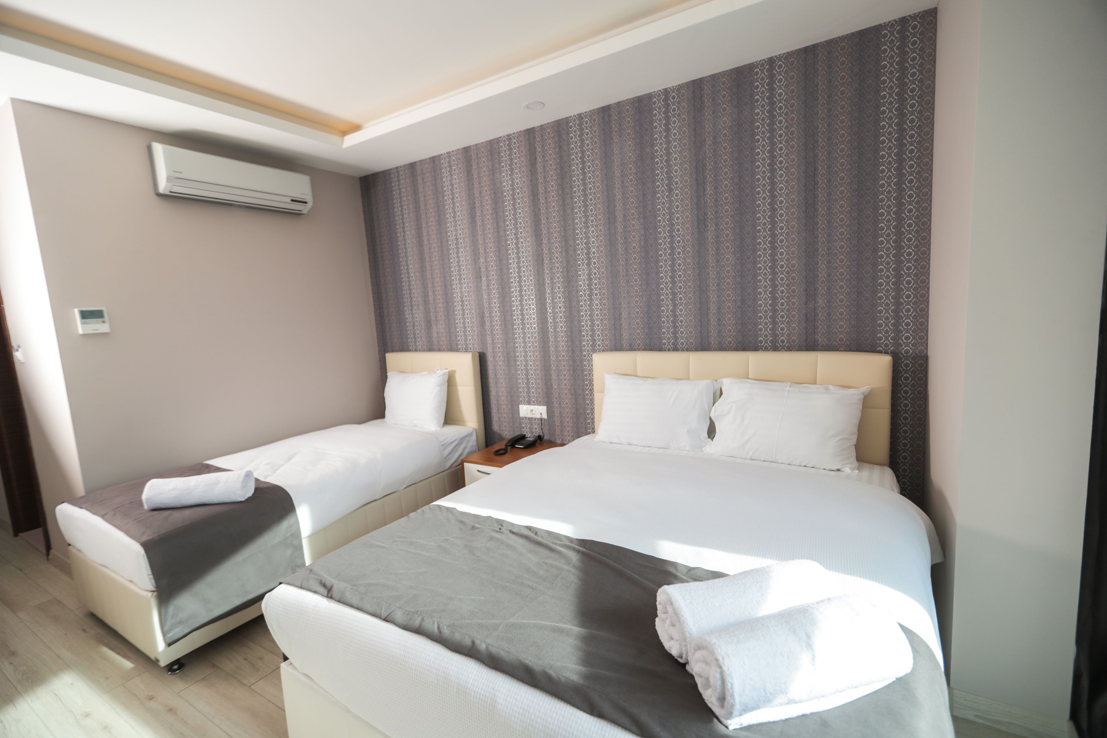 Ein Hotelzimmer mit zwei Einzelbetten, einem großen Bett, einem Nachttisch mit Telefon und einer Klimaanlage an der Wand.