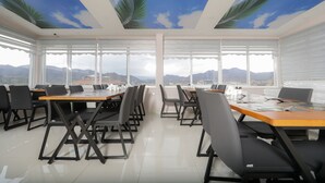 A conference room with tables and chairs, large windows with a view of mountains, and a ceiling with a sky and palm tree design. - Grand Dost Hotel (Osmancik)