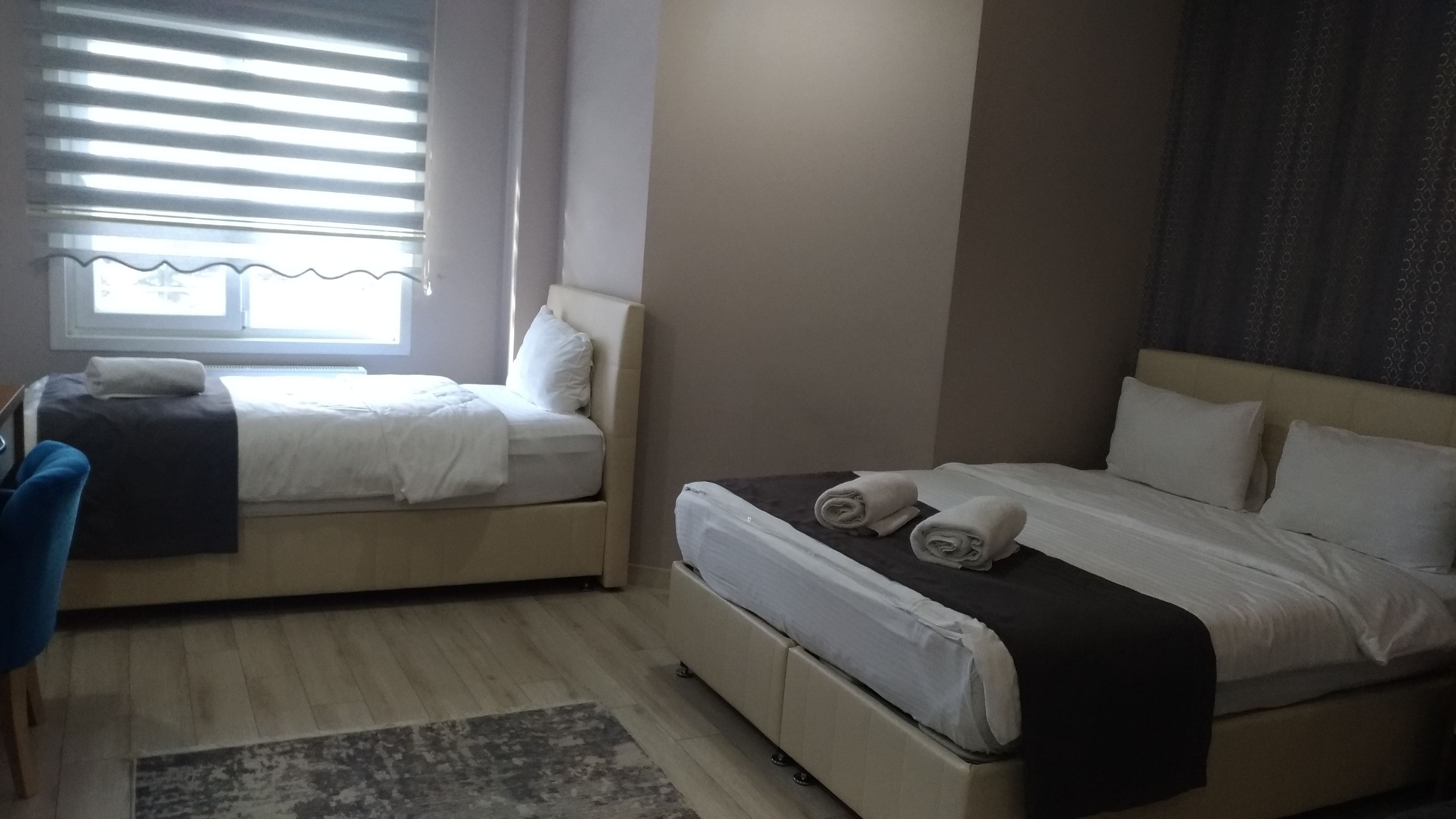 A hotel room with two beds, a desk, and a window with blinds.