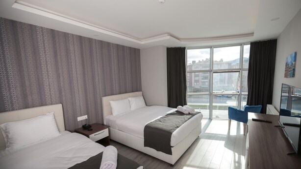 A hotel room with two beds, a desk, and a large window offering a city view. - Grand Dost Hotel (Osmancik)