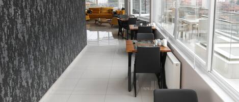 Uma área de refeições moderna em hotel, com teto alto, amplas janelas e vista para a cidade.