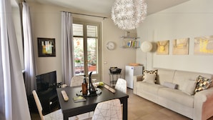 A modern living room with a sofa, dining table, and a TV. There are artworks on the wall and a decorative light fixture. - Via Cavour Appartamenti (Alba)