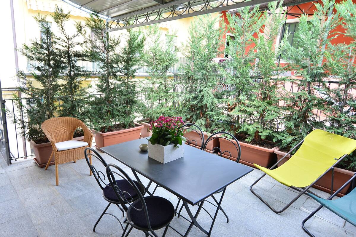 A patio area with a table and chairs, surrounded by potted plants and a decorative wall.
