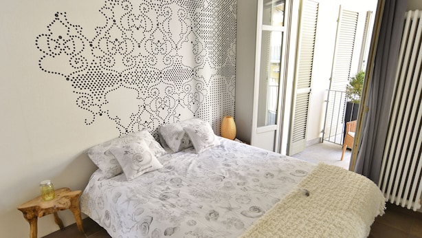 A bedroom with a bed, a nightstand, a decorative wall, and a view of the outside. - Via Cavour Appartamenti (Alba)