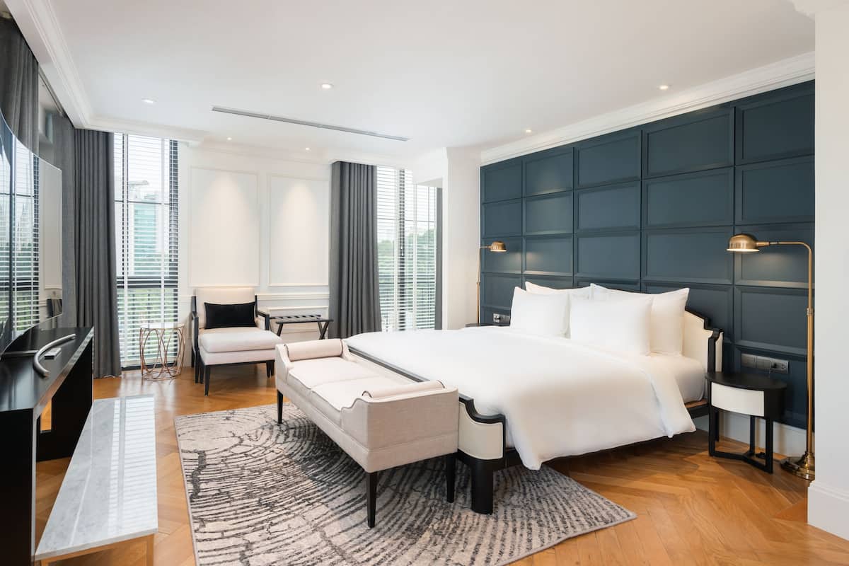A modern hotel room with a large bed, a desk, a chair, and a TV.