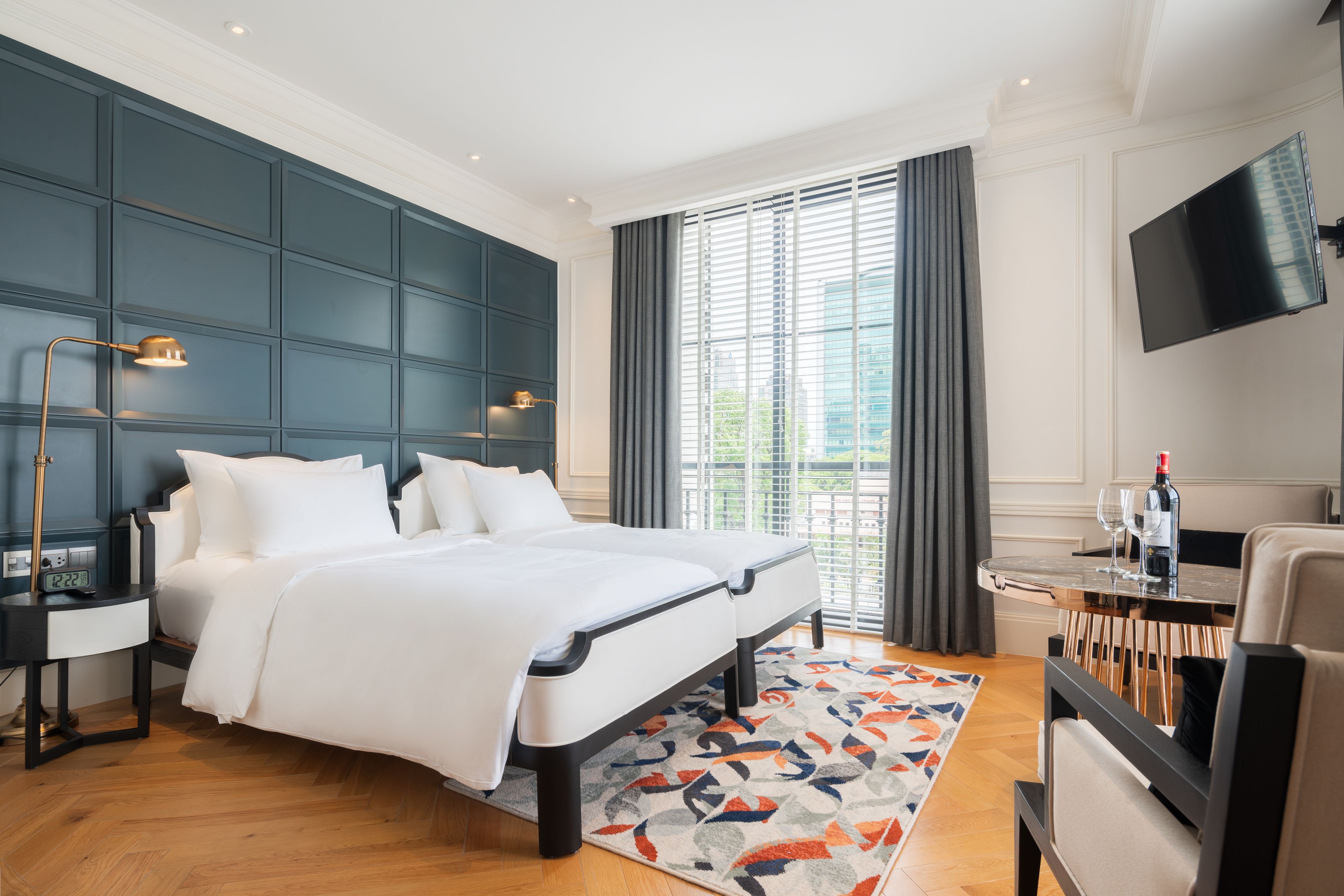 A modern hotel room with a large bed, a desk with a chair, a flat-screen TV, and a window with curtains.