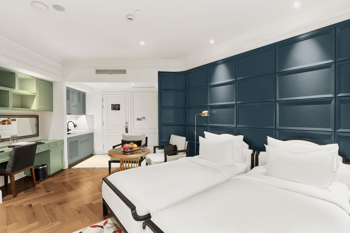 A modern hotel room with a large bed, a desk, and a kitchenette.