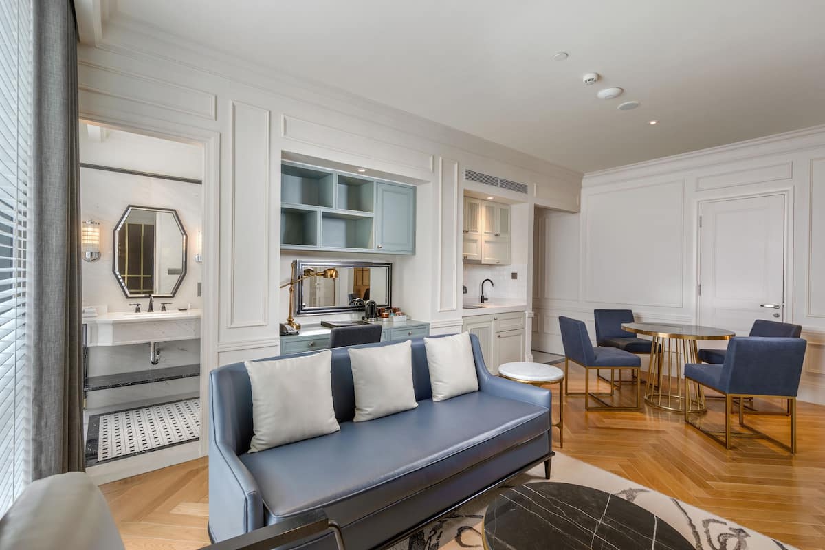A modern living room with a blue sofa, a dining area with blue chairs, and a kitchen with white cabinets.