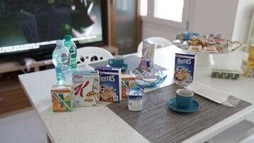 Une table de petit-déjeuner avec divers aliments et boissons, notamment des boîtes de céréales Frosties et Kellogg's Special K, une tasse bleue et une bouteille d'eau.