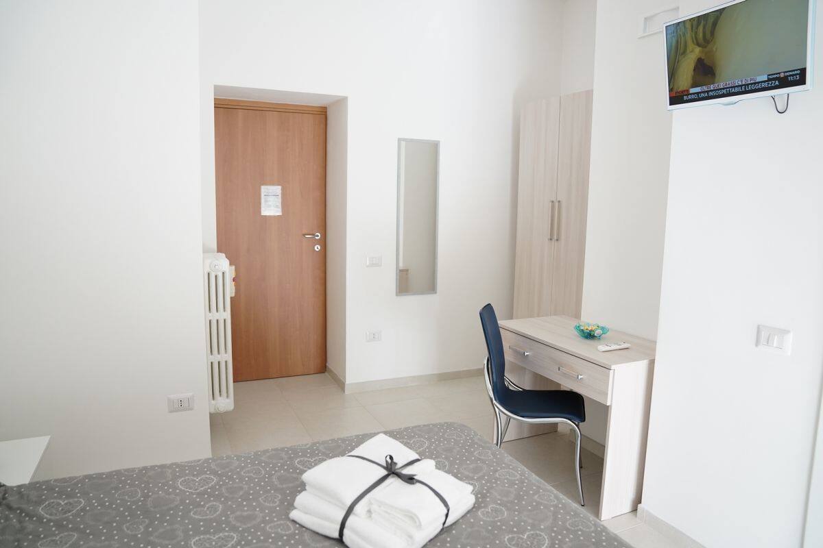 A hotel room with a bed, a desk, a chair, a wardrobe, and a television on the wall.