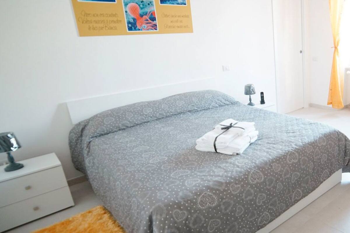 A bedroom with a bed, bedside table, lamp, and a window with curtains.