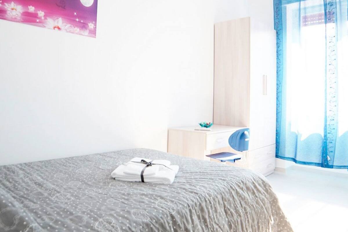 A bedroom with a bed, a bedside table, a wardrobe, and a window with curtains.