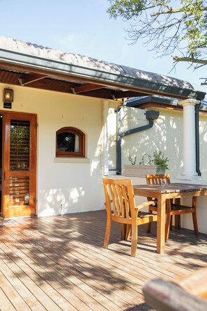 A wooden deck with a table and chairs, a potted plant, and a window with a view of trees. - Lovane Boutique Wine Estate & Guesthouse (Stellenbosch)