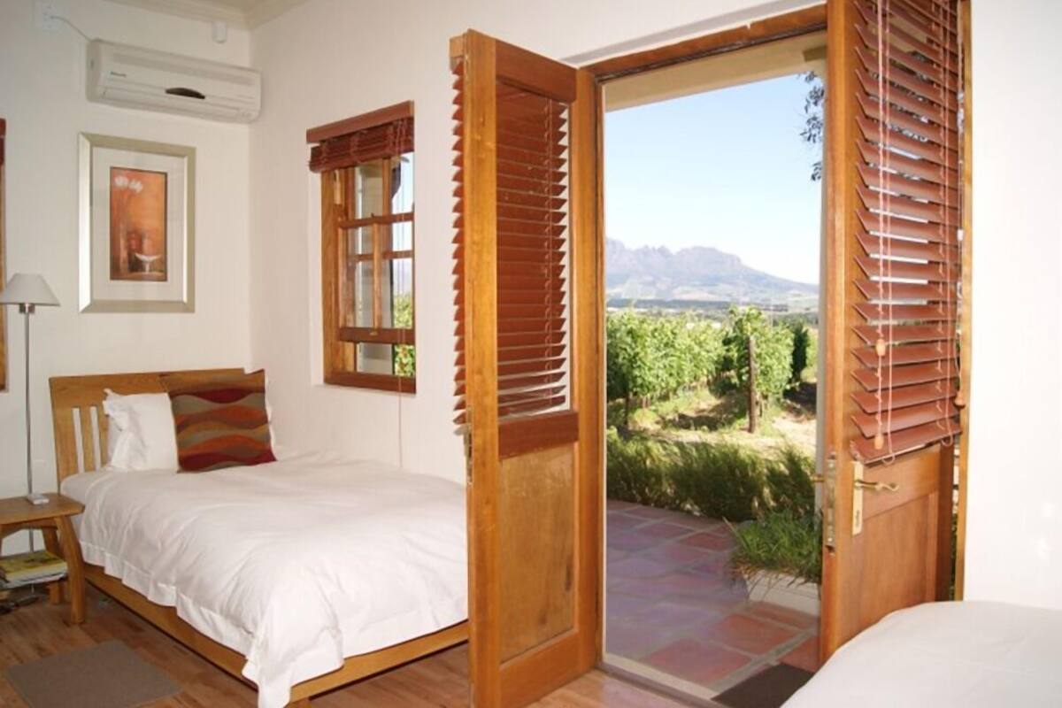 Ein Schlafzimmer mit einem Bett, einem Nachttisch, einem Fenster mit Jalousien und Blick auf einen Weinberg.