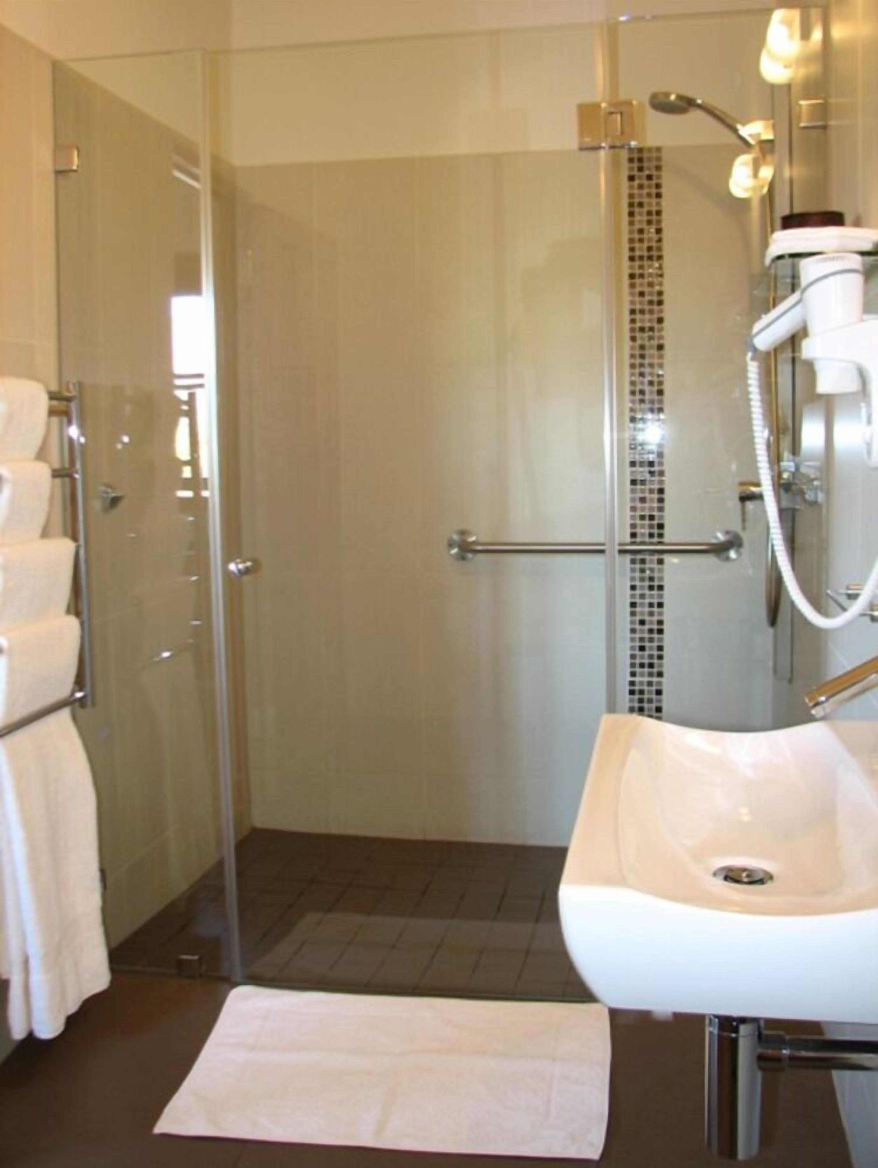 Un baño moderno con cabina de ducha de vidrio, lavamanos blanco y zona de ducha con azulejos.