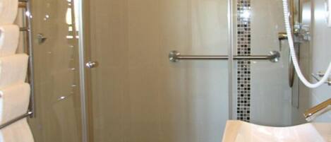 Un baño moderno con cabina de ducha de vidrio, lavamanos blanco y zona de ducha con azulejos.