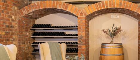 A cozy wine cellar with brick walls, wine racks, comfortable seating, and a large wooden barrel.