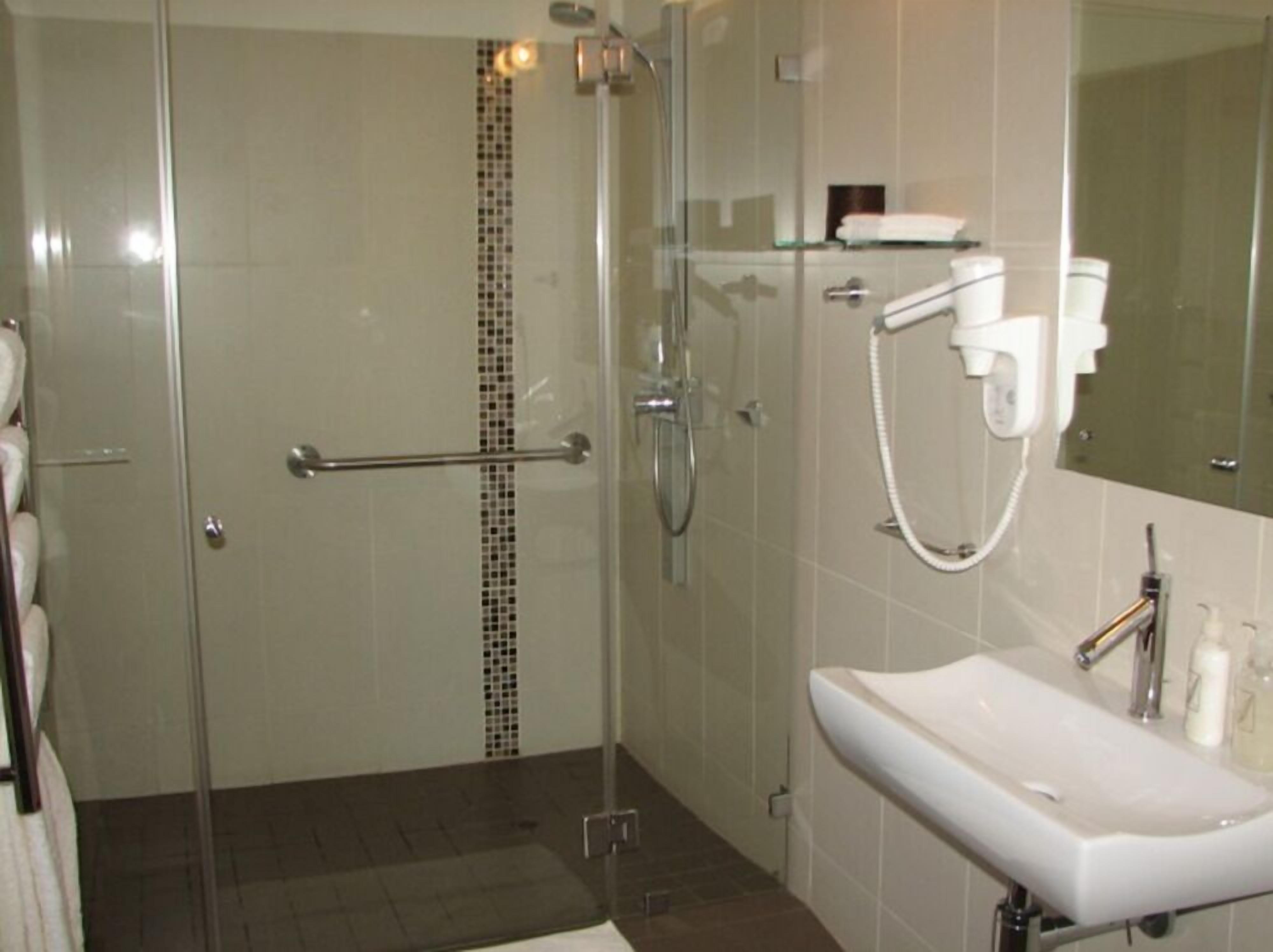 A modern bathroom with a glass shower enclosure, a white sink, and a mirror above it.