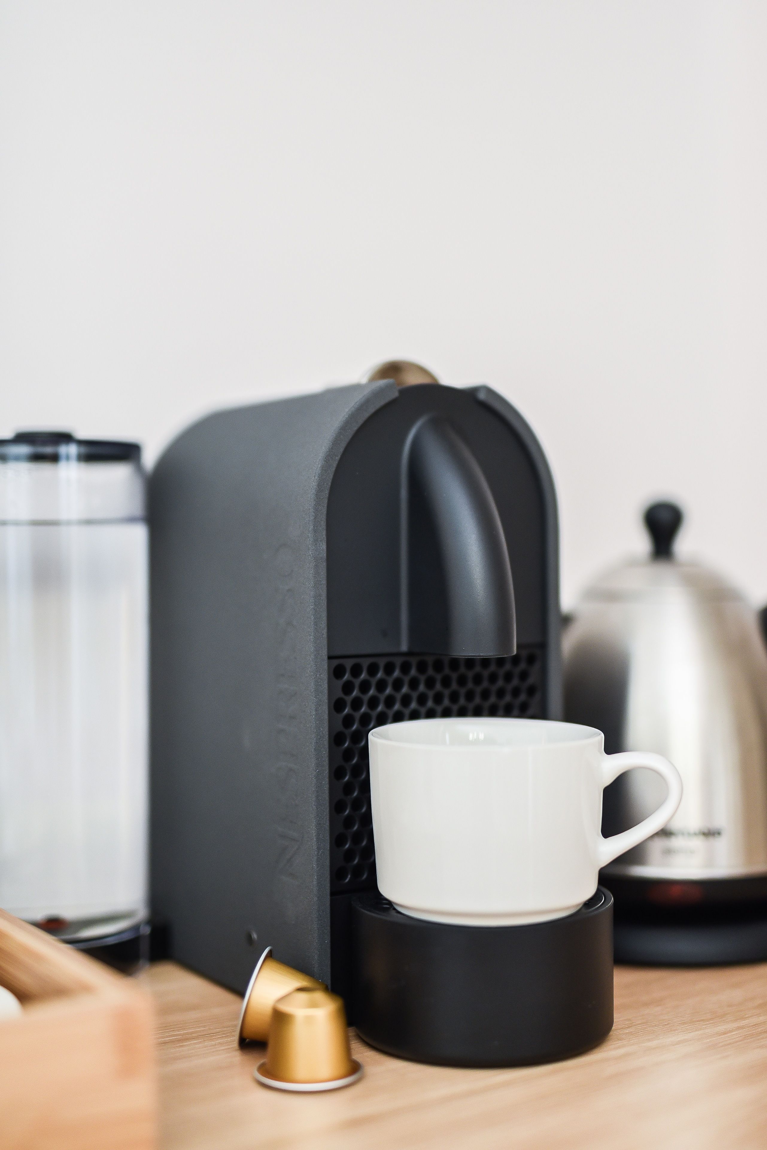 Une machine à café, une tasse blanche et un pot en argent sur une surface en bois.