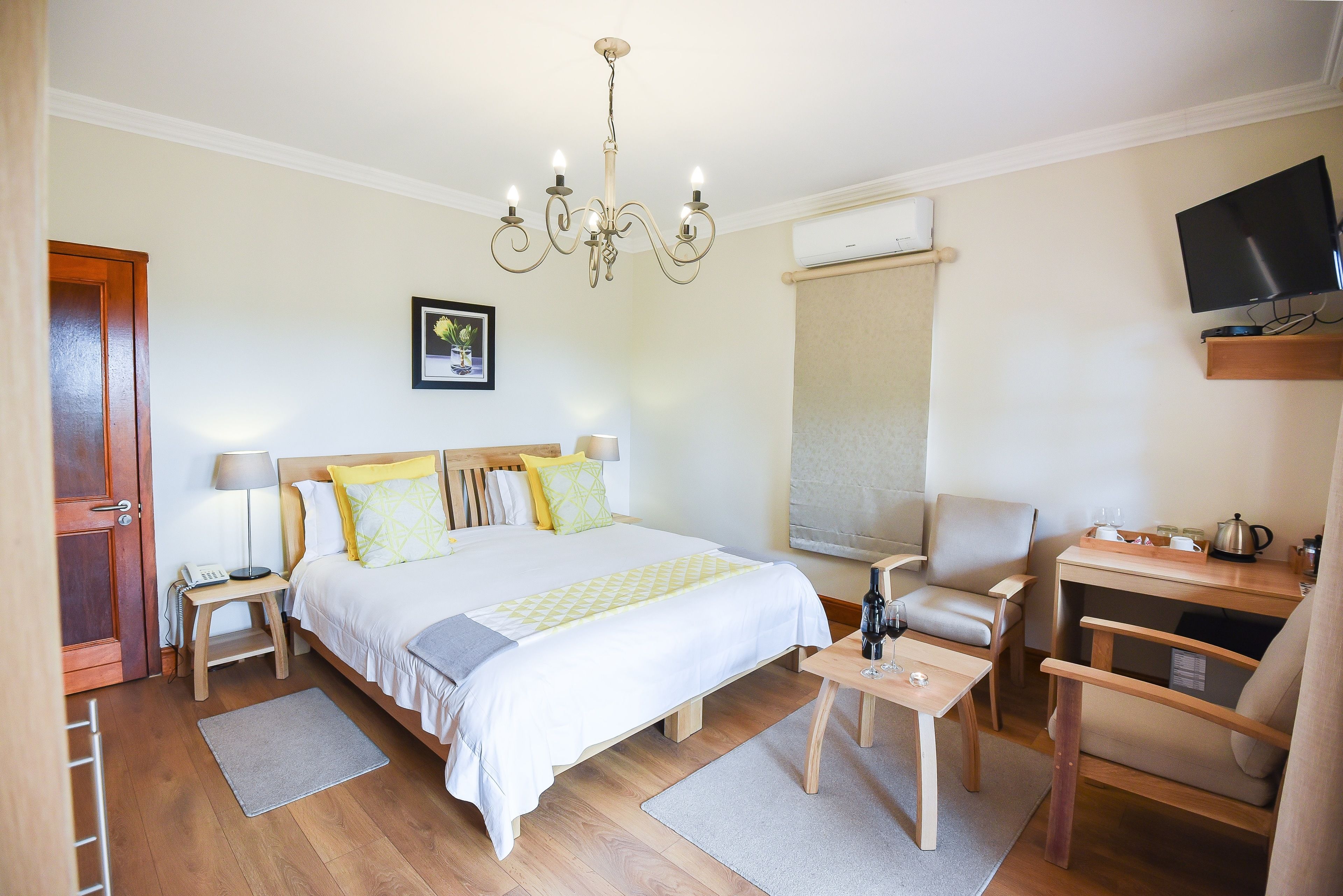 A hotel room with a bed, bedside tables, a desk, a chair, a TV, and a chandelier.