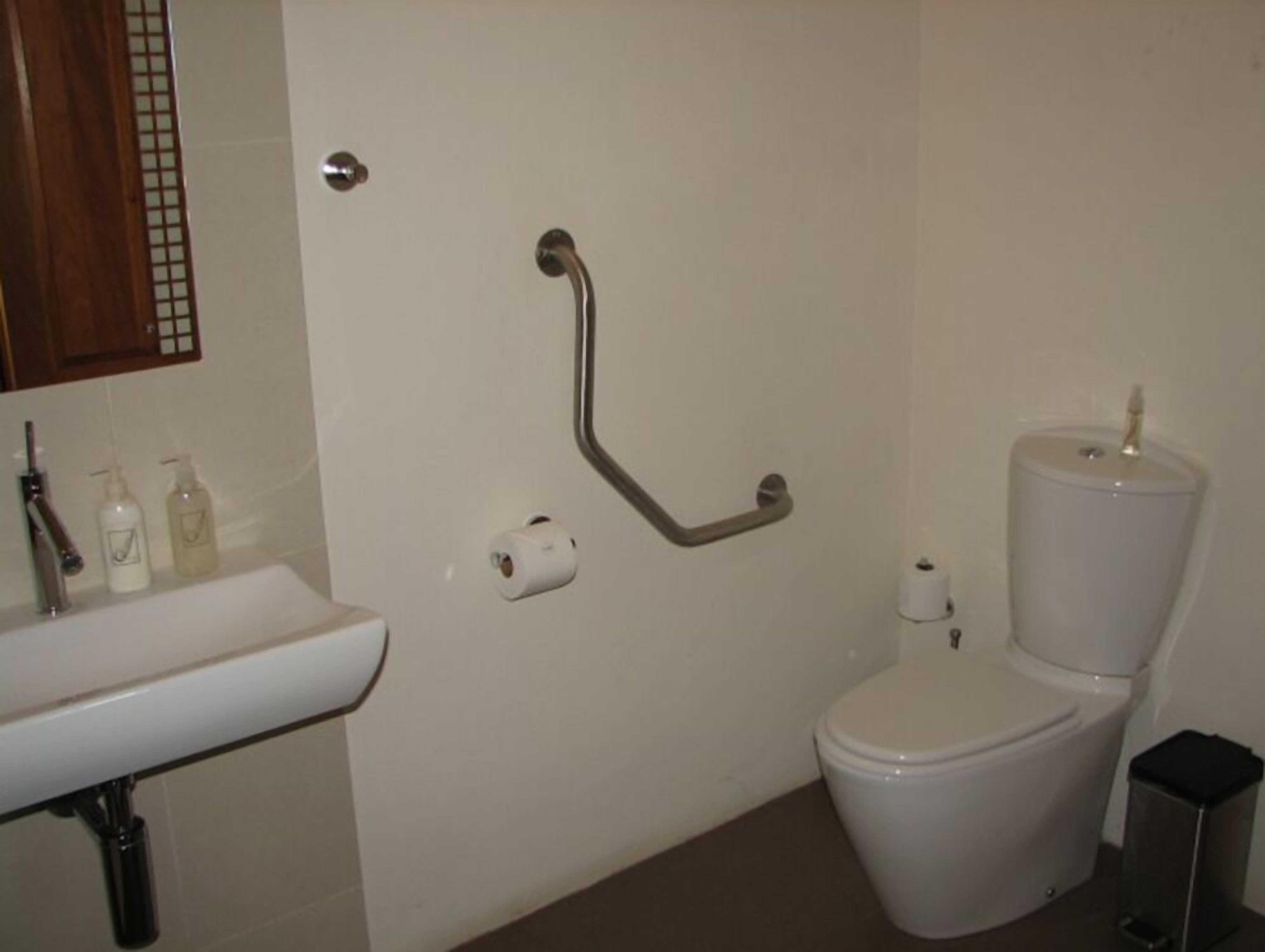 A bathroom with a white sink, toilet, and a grab bar on the wall.