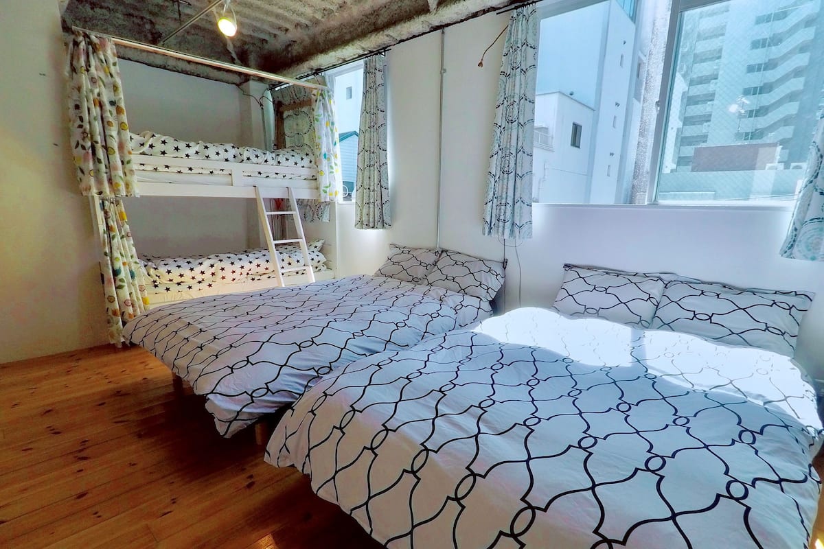 A bedroom with a bunk bed, a single bed, wooden flooring, and a window with curtains.