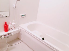 A bathroom with a white bathtub, a toilet, and a shelf with toiletries.