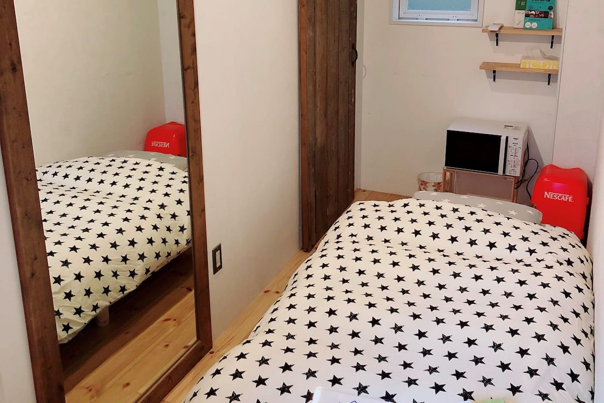 A bedroom with two beds, a wooden floor, a mirror, a window, a microwave, and a Nescafé coffee maker.