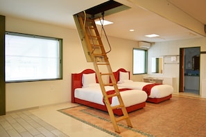 Une chambre d’hôtel avec deux lits, une échelle en bois, un bureau et une salle de bain visible à travers une porte ouverte.