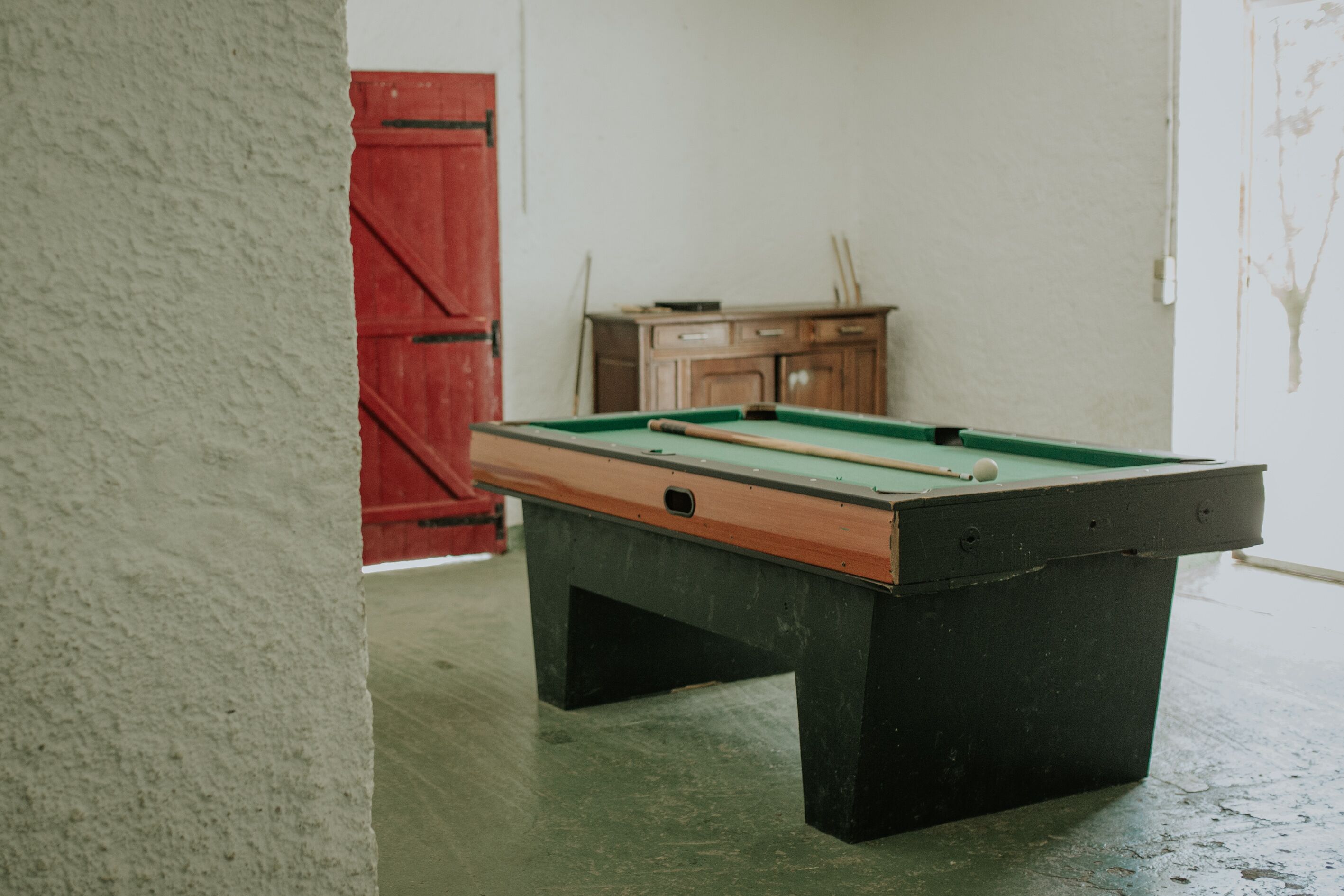 Una mesa de billar en una habitación con una puerta roja y un armario al fondo.