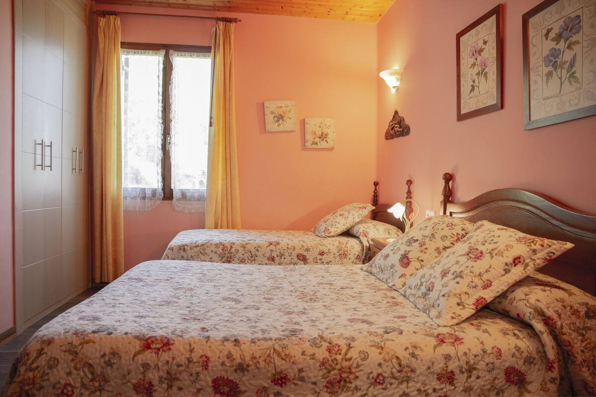 A bedroom with two beds, floral bedding, a wardrobe, and wall-mounted artwork.