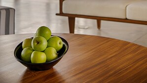 A room with a wooden table, a bowl of green apples, a sofa, and a view through large glass doors. - Jetwing Villa 700 (Induruwa)