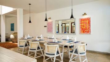 A dining area with a long table, chairs, hanging pendant lights, and wall art.