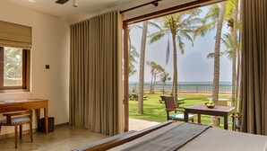 A hotel room with a bed, a desk, and a view of the ocean and palm trees. - Jetwing Villa 700 (Induruwa)