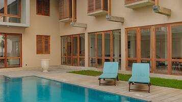 Una casa moderna con piscina, ventanas amplias y un patio con sillones de descanso.
