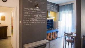 Une cuisine chaleureuse avec un mur recouvert d’un tableau noir, un coin repas avec une table et des chaises, et une fenêtre avec des rideaux.
