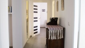Un couloir avec un plancher en bois, une porte blanche au fond et une petite table avec une lampe.