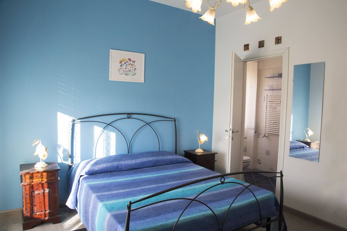 Een slaapkamer met een bed, nachtkastjes, een spiegel en een deur naar de badkamer.