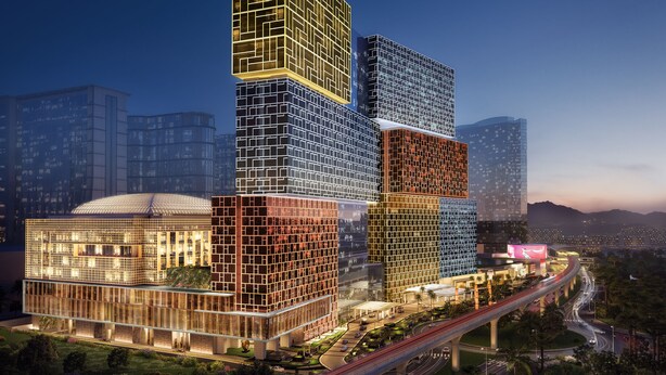 Un moderno edificio de varios pisos con una fachada geométrica distintiva, rodeado de vegetación y conectado por un puente.